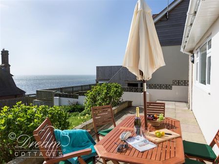 An outdoor patio with a wooden table and chairs an umbrella fruit basket and ocean view at Seacliff in West Bay