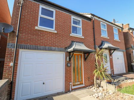 A brick house exterior with two white garage doors two upper windows and two front doors with canopies at Sea Pebbles in Weymouth