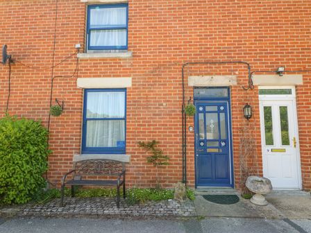 The exterior of a brick house with a blue door numbered 8 and a white door numbered 9 a metal bench two windows and some plants at Studland Cottage in Studland