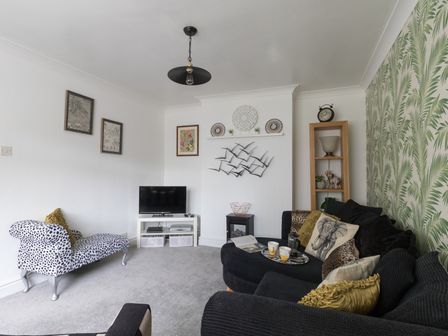 A living room with a TV on a white stand and a black sofa with animal print cushions at Sunny Days in Weymouth