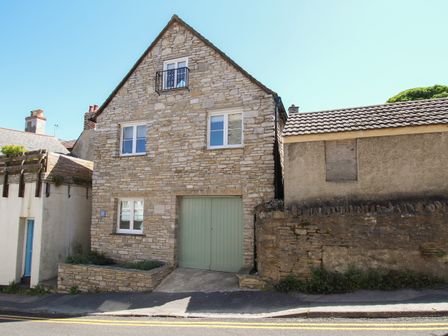 A stone house with green garage doors and white windows next to a building with a boarded-up window at Swanage Driftwood in Swanage