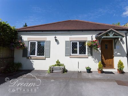 Exterior of a single story cottage with two windows and a wooden door with plants in pots outside at Toll Lodge in Frampton