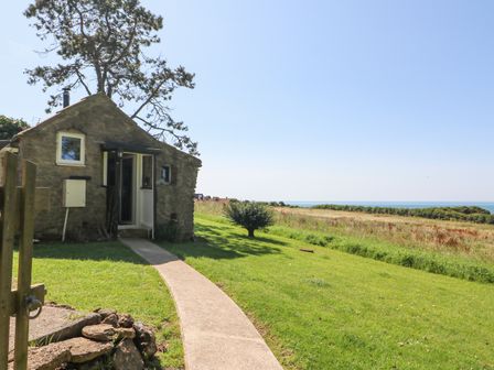 A stone cottage with a path leading to the door and a grassy field with a tree and sea in the background at Washingpools in West Bexington