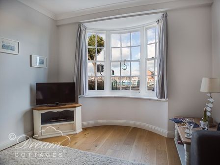 A corner of a living room with a bay window showing a view outside and a TV on a white cabinet at Waterside in Weymouth