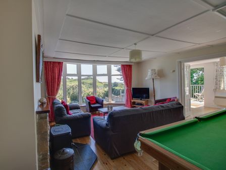 A living room with sofas and a pool table next to large windows with red curtains at Waterson in Osmington