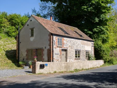 A stone and brick cottage with a tiled roof and a small garden beside a road at Way's Forge in Piddlehinton