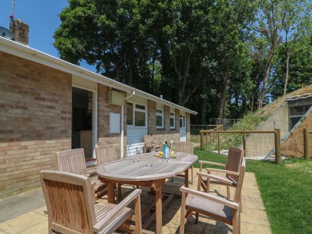 An outdoor patio with wooden table and chairs in a grassy area beside a brick building at Woodlands Cottage in Ringstead