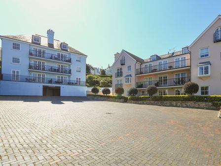 An outdoor paved parking area in front of modern multi-story residential buildings with balconies and trimmed trees at 15 Combehaven in Salcombe
