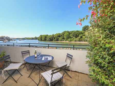 An outdoor patio with a round table and four chairs overlooking a river with boats and trees at 1 Crabshell Quay in Kingsbridge