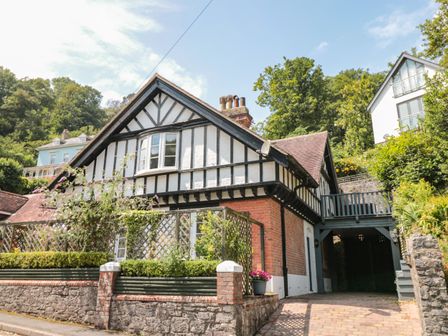 An exterior view of a Tudor style house with a brick and timber facade and surrounding greenery at 1 The Old Coach House in Dartmouth