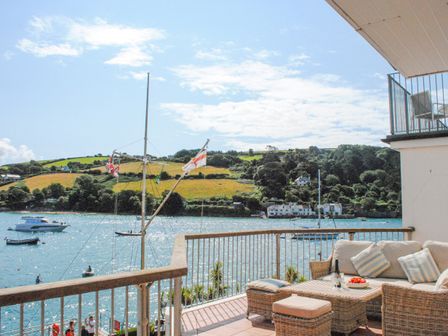 A balcony with wicker furniture and cushions overlooking water boats and green hills at 22 The Salcombe in Salcombe