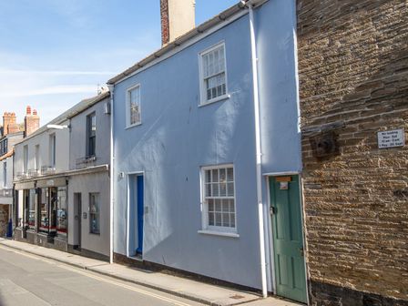 A street view with a row of attached buildings including a blue house with white windows and doors at 29 Fore Street in Salcombe