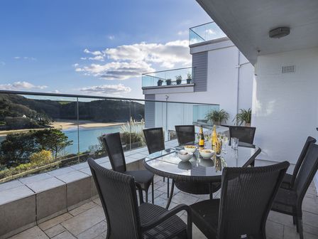 A balcony with a glass table set for drinks and snacks overlooking a beach and hills at 2 Hamstone Court in Salcombe
