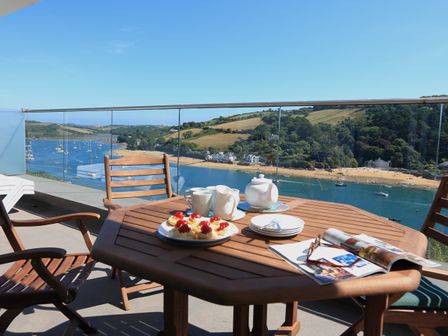 A balcony with a wooden table and chairs overlooking a river with boats and a beach at 2 Poundstone Court in Salcombe