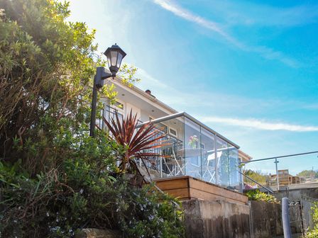 A glass balcony with a white table and chairs outside a house with plants and a street lamp at 2 Rockmount in Salcombe