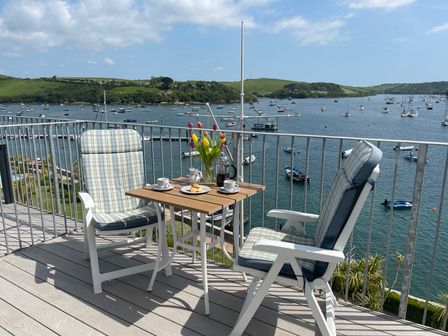 A balcony with two chairs and a table set with coffee cups and flowers overlooking a harbor with boats at 36 The Salcombe in Salcombe