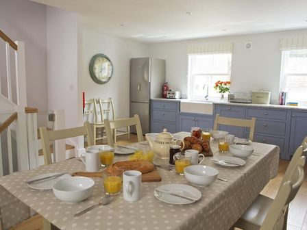 A kitchen and dining area with a table set for breakfast and blue cabinets at 3 Eddystone Row in Salcombe