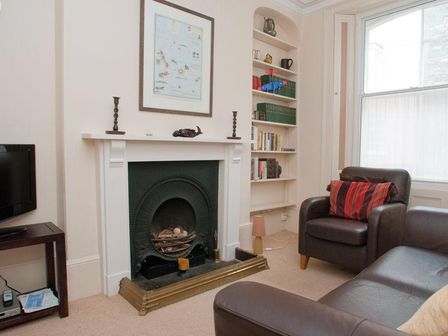 A living room with a fireplace a leather armchair with a cushion a brown sofa a TV on a stand and shelves with books at Aeolus House Dartmouth