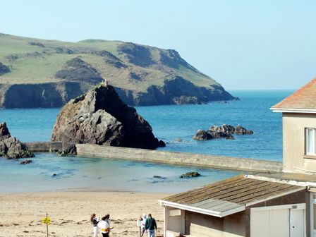 A beach with people walking near a building and rocky cliffs by the sea at 4 Armada House in Hope Cove