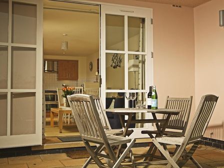 A patio with a wooden table and four chairs and bottles on the table at 4 Combehaven in Salcombe