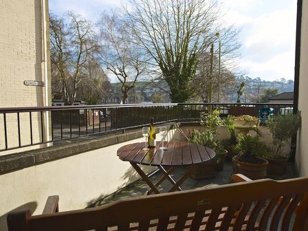 A balcony with a wooden table and two wine glasses with plants along the wall at 4 Dartmouth House in Dartmouth