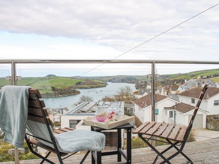 A balcony with two wooden chairs and a small table with a tea set overlooking houses and a river at 4 Lyndhurst in Salcombe