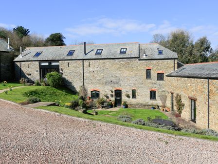 A stone building with multiple windows and doors surrounded by grass and outdoor seating at Cowslip Cottage in Frogmore