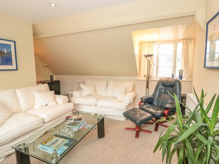 A living room with two white sofas a black leather armchair with footrest a glass coffee table with books and a green plant at 5 Island Street in Salcombe