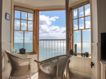 A small seating area with two wicker chairs facing windows overlooking the sea at 5 Prospect House in Hallsands
