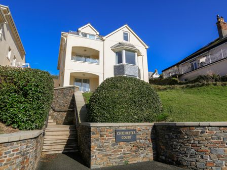 The front exterior of a multi-story white building with steps and stone walls labeled Chichester Court in Hope Cove