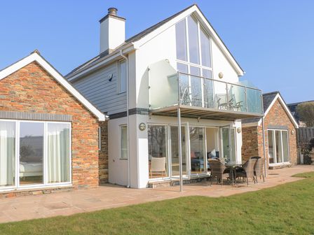 A two-story house with glass balcony and outdoor seating on a patio with grass at Sea Peep in Thurlestone