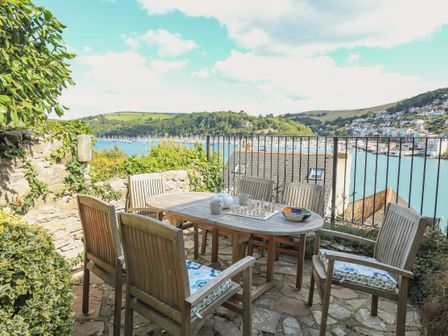 An outdoor patio with a wooden table and six chairs overlooking a body of water and hills at 7 Nelson Steps in Dartmouth