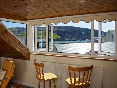 A room with wooden chairs facing an open window overlooking hills and water at 8 Church Street in Salcombe