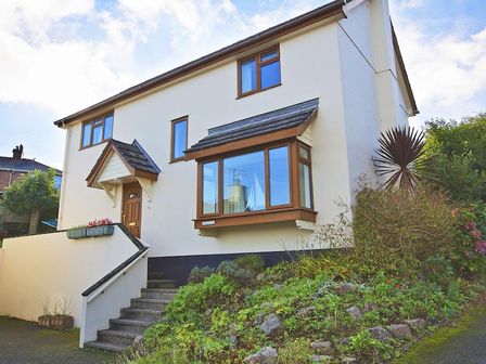 A two story house with a front door porch and a bay window with plants on the slope at Amberley in Dartmouth