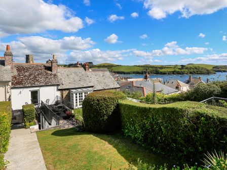A garden with trimmed hedges and lawn overlooking rooftops and a body of water at Aune Cottage in Salcombe