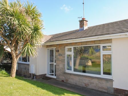 The exterior of a single-story house with a white door and large window and a tree on the lawn at Bankside in Hope Cove