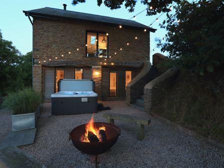 An outdoor space with a fire pit bench hot tub string lights and a stone house at The Bothy in Slapton