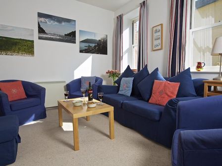 A living room with blue sofas and armchairs a wooden coffee table with wine glasses and snacks and picture frames on the wall at Columbine in Dartmouth
