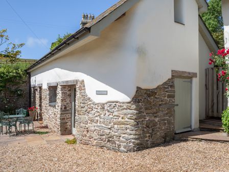 A stone and plaster cottage with a green door and outdoor metal table and chairs at Cola's Tonne in Malborough
