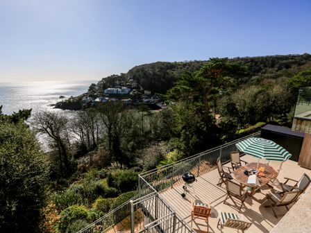 A terrace with a table and chairs under a striped umbrella overlooking a wooded hillside and coastline at Courtenay Villa in Salcombe