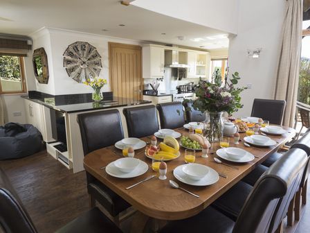 A dining room with a wooden table set for breakfast and an open kitchen at Court Lodge Hillfield Village in Dartmouth