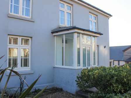 The exterior of a house with multiple white framed windows and a small porch surrounded by bushes and plants at Cindys Retreat in Hope Cove