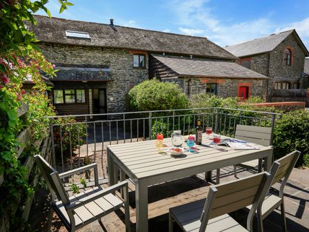 An outdoor patio with a table and four chairs with drinks and snacks on the table outside stone buildings at The Granary Malborough