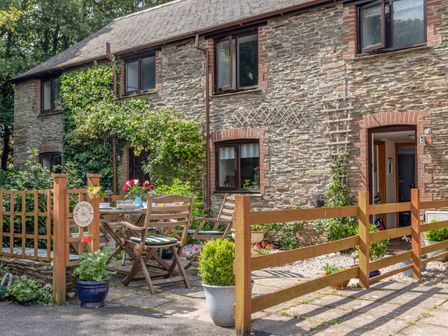 A stone cottage exterior with wooden fence and outdoor seating at Honeysuckle Cottage in Bigbury