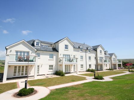 A white multi-unit building with balconies and glass railings overlooking a lawn with circular walkways at Horizon in Thurlestone