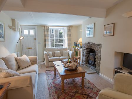 A living room with sofas a wooden coffee table a stone fireplace and a window with curtains at Jot Cottage in Salcombe