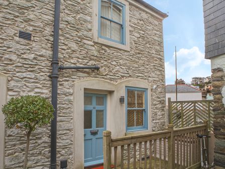 Exterior stone wall of a house with blue door and windows small tree and wooden fence at Lee Shore in Salcombe