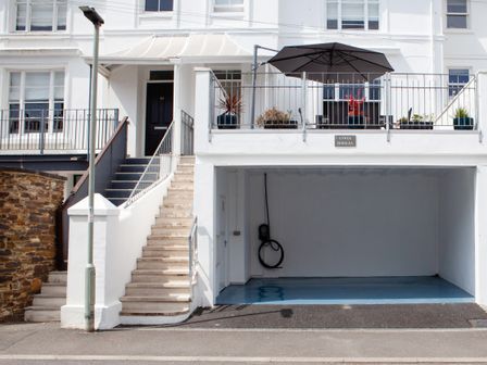 A white building with outdoor stairs leading to a black door and a covered garage below with an electric vehicle charging point at Lower Fernlea in Salcombe