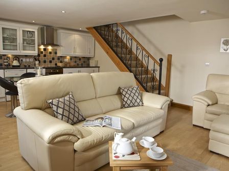 A living room with beige sofas a wooden staircase and a kitchen area at Meadow View in Modbury