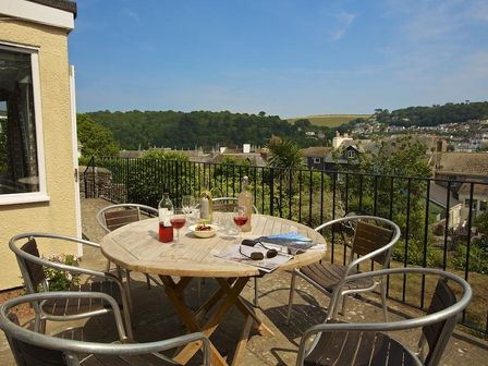 An outdoor patio with a round wooden table and four metal chairs overlooking houses and hills at Moonrakers Clarence Street in Dartmouth